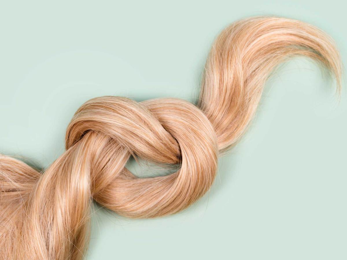 Blonde Haarstr&auml;hne zu einem Knoten gebunden. Str&auml;hne von honigblondem Haar auf mintfarbenem Hintergrund, Ansicht von oben. Friseur Service, Haar St&auml;rke, Haarschnitt, Frisur, F&auml;rben oder F&auml;rben, Haarverl&auml;ngerung, Behandlung Konzept.
