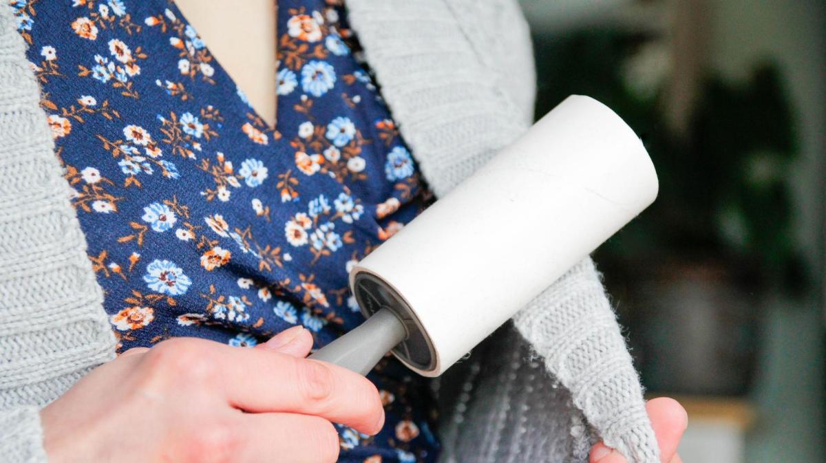 Frau entfernt Fusseln auf einer Strickjacke mit einer Fusselrolle.