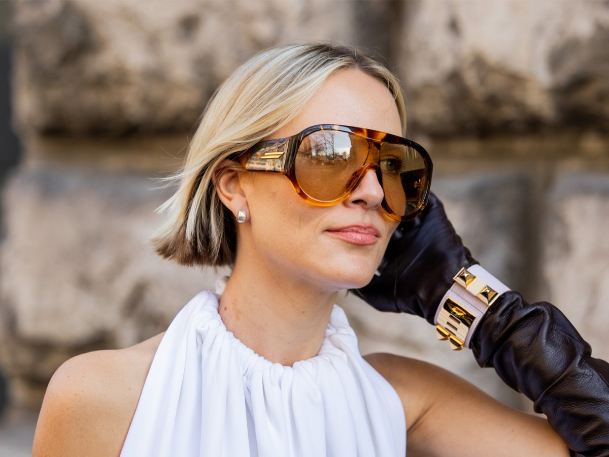 Frau im androgynen Look mit Sonnenbrille und kurzer Bob-Frisur.