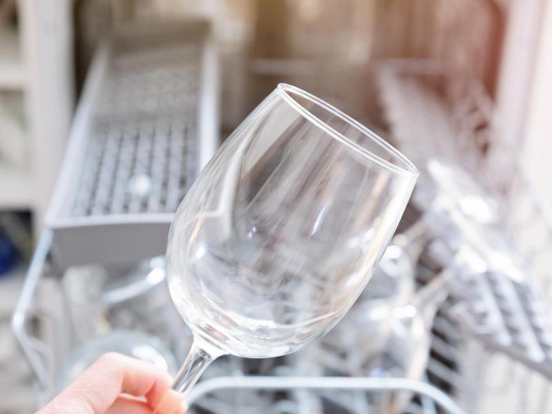 Frau holt ein milchiges Weinglas aus der Spülmaschine.