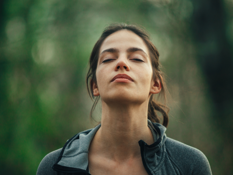 Frau steht mit geschlossenen Augen in einem Wald