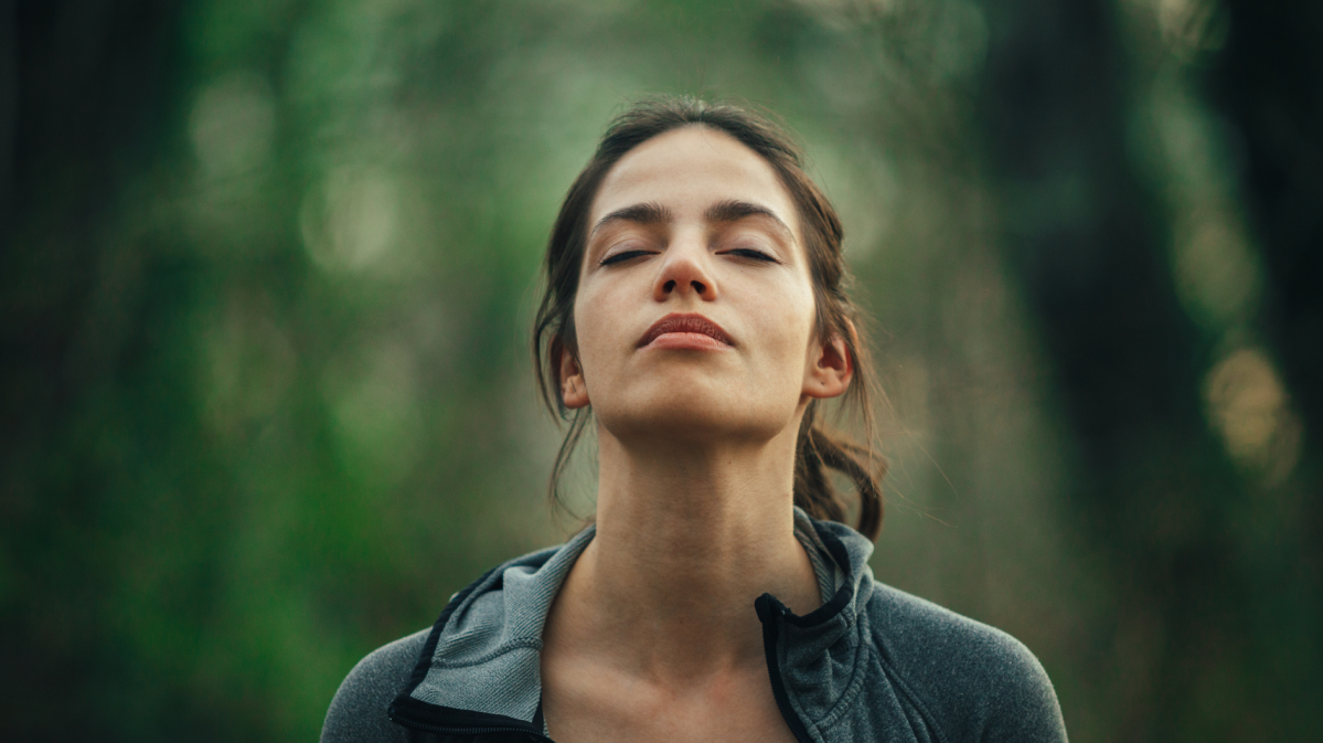 Frau steht mit geschlossenen Augen in einem Wald