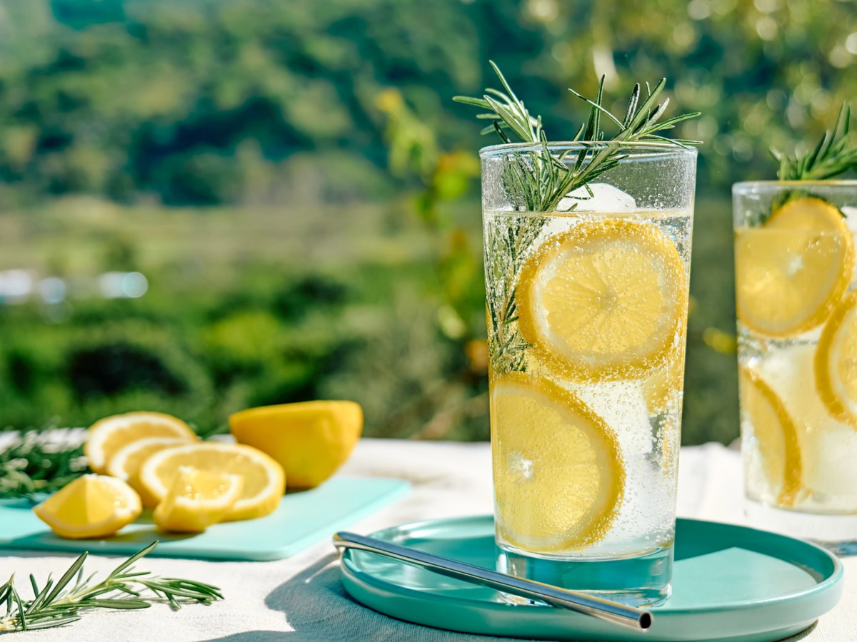 Zwei Cocktailgl&auml;ser mit Zitronenscheiben auf Tisch mit sommerlichem Hintergrund.