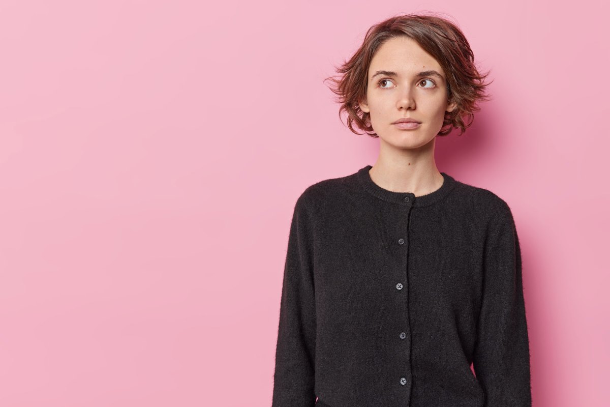 Frau vor einer pinken Wand blickt ernst zur Seite