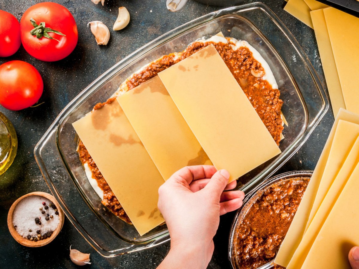 Person bereitet Lasagne zu.