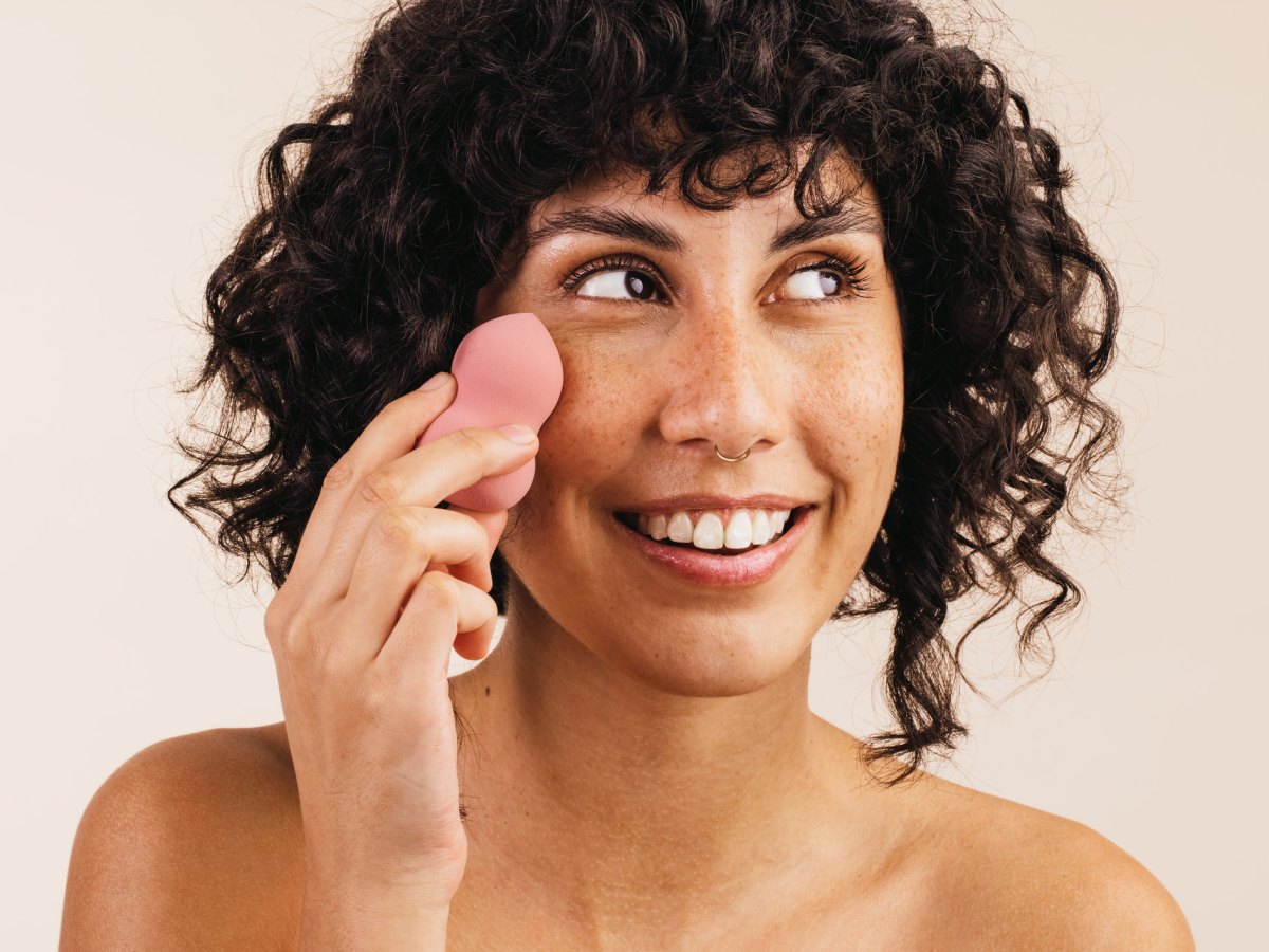 Frau mit lockigem braunen Haar benutzt rosa Beauty Blender