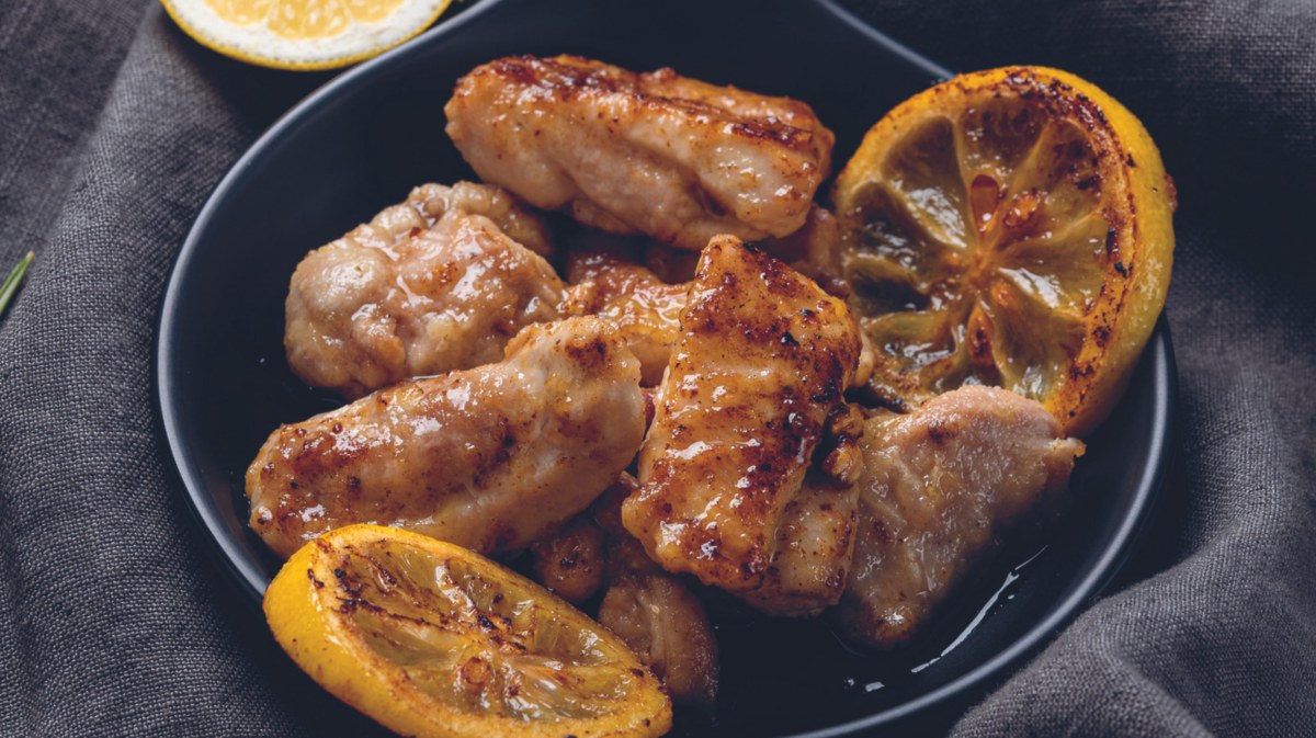 Italienisches Pollo al limone auf einem schwarzen Teller.