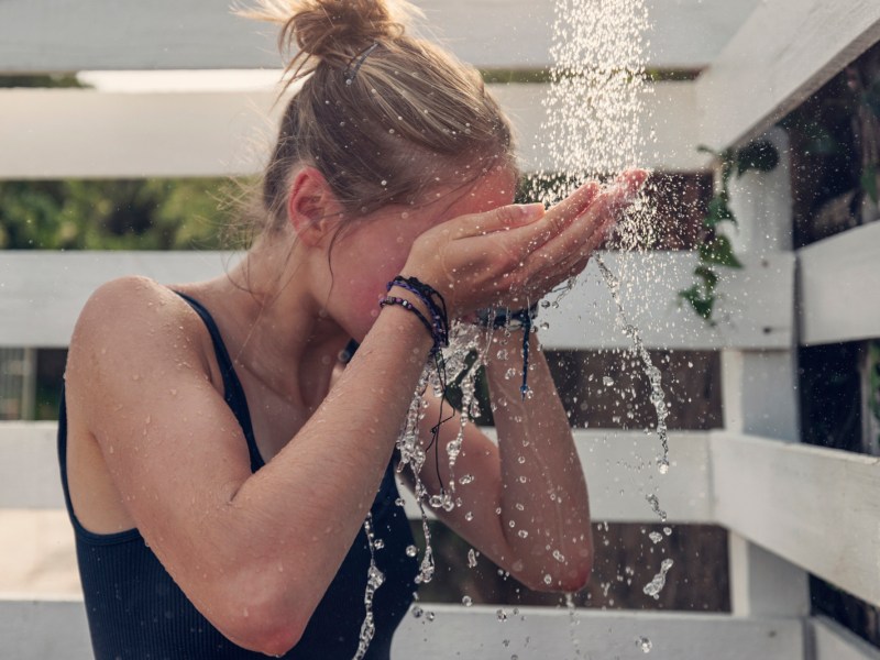 Frau duscht sich im Freien und erfrischt sich bei Hitze.