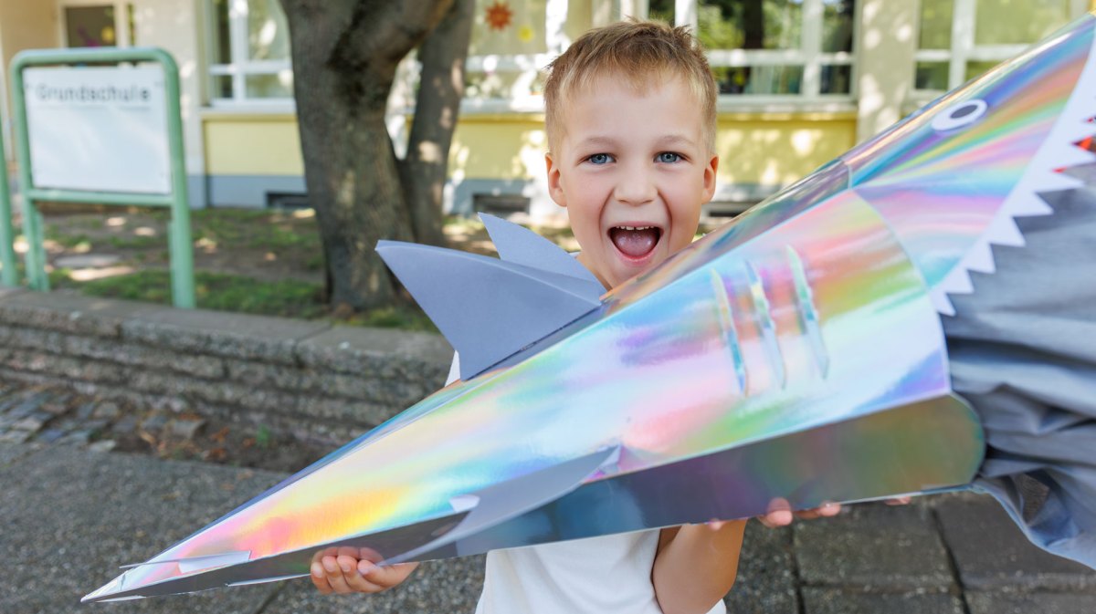 Junge an seinem ersten Schultag mit einer Schultüte in Hai-Form.