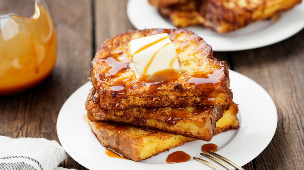 Arme Ritter auf einem weißen Teller, mit einem Butterstück und Sirup getoppt.