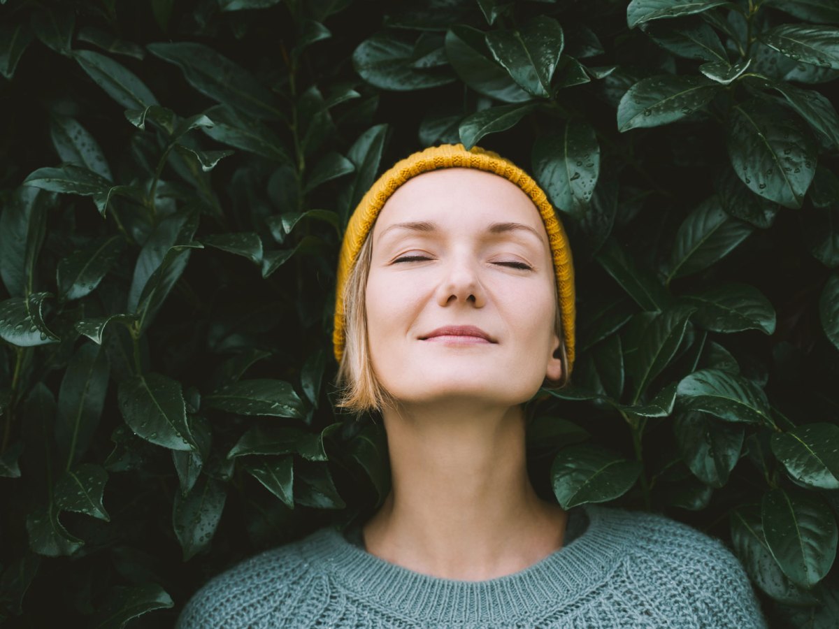 Frau lehnt mit geschlossenen Augen an einem Busch