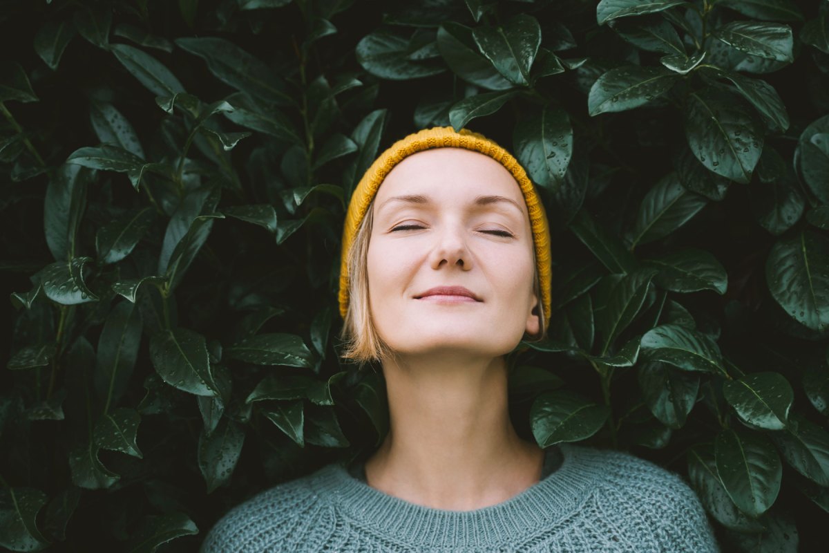 Frau lehnt mit geschlossenen Augen an einem Busch