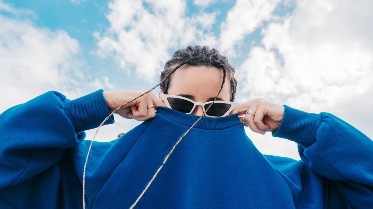 Frau mit Sonnenbrille versteckt ihr Gesicht in ihrem Pullover