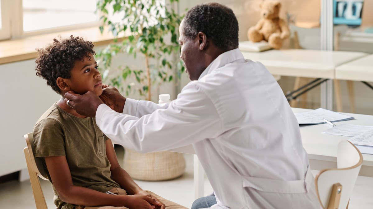 Junge sitzt bei Arzt, der den Hals des Kindes abtastet.