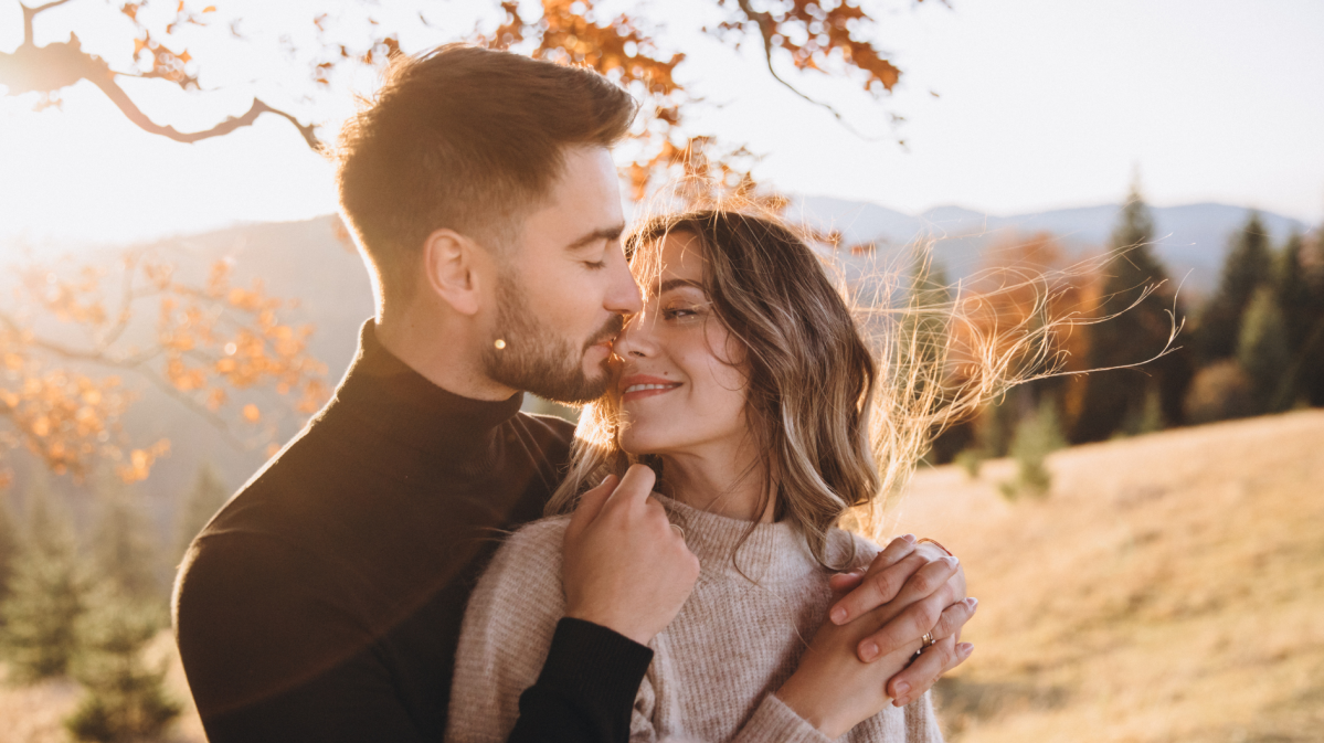 Frau und Mann vor einem Laubbaum, die sich verliebt angucken und im Arm halten.