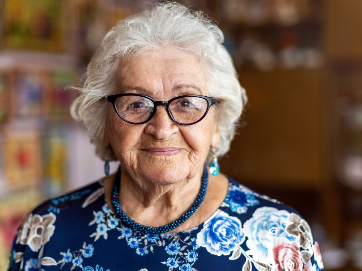 Porträt einer alten Frau, die freundlich in die Kamer lächelt.