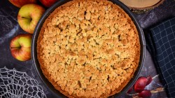 Apfelkuchen mit Streusel von oben, daneben liegen Äpfel.