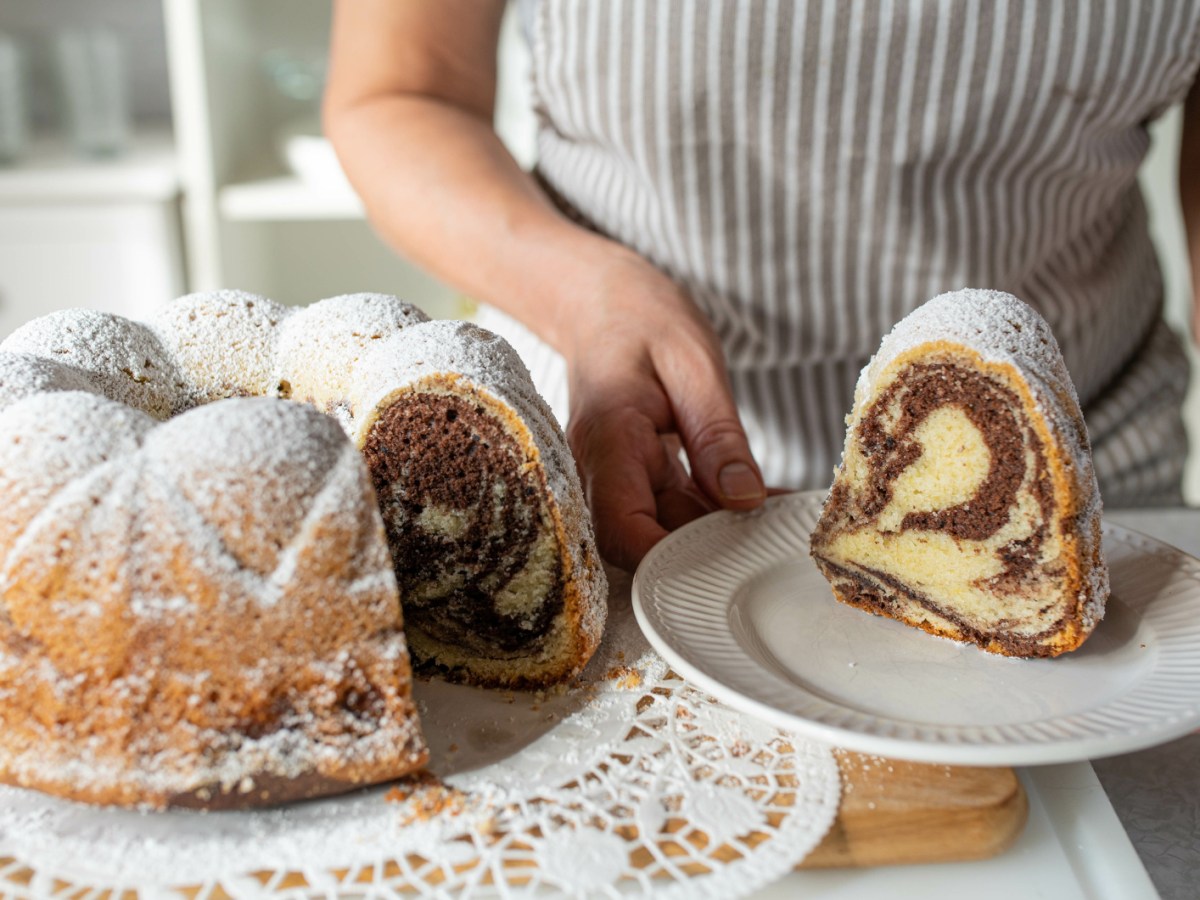 Person hat St&uuml;ck Gugelhupf auf Kuchenteller.