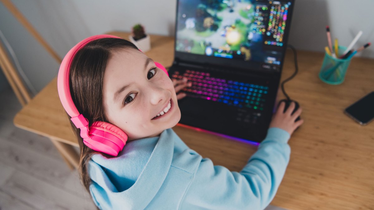 Mädchen, ca. 10 Jahre alt, sitzt mit Kopfhörern am Laptop und spielt darauf.