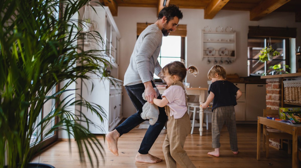 Vater tanzt mit seinen beiden Kindern in einer Wohnung im skandinavischen Stil.