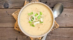 Kartoffelsuppe mit Lauch in einer hellen Sch&uuml;ssel auf einem Holztisch.