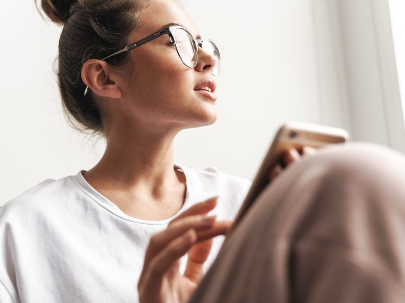 Frau mit Brille sitzt auf dem Sofa mit einer Decke über den Beinen und schaut aus dem Fenster