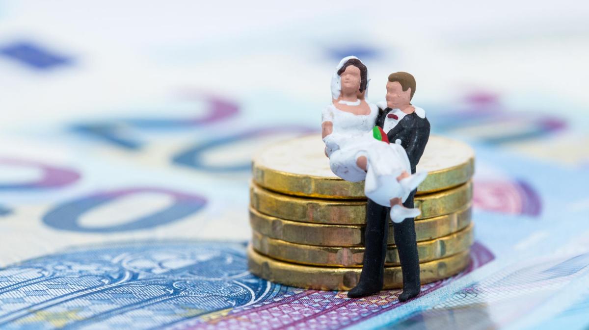 Kleine Brautpaarfiguren stehen auf Geldscheinen und neben einem Münzturm.