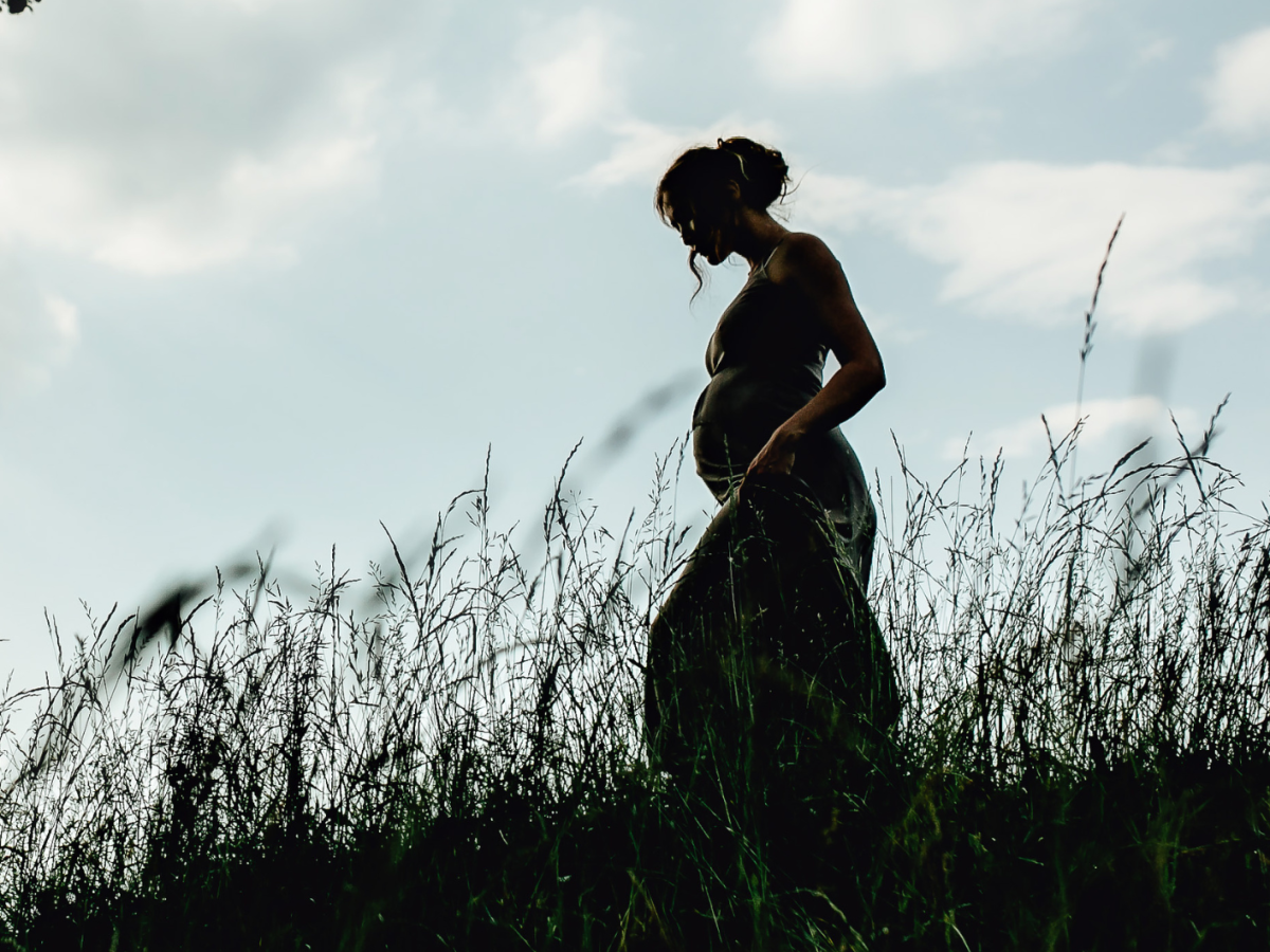 schwangere Frau vor einem Sonnenuntergang über dem Meer