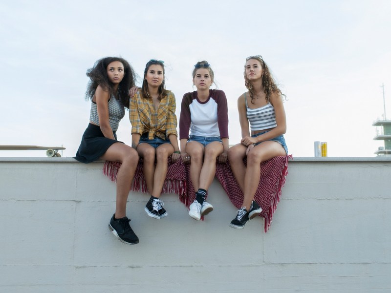 Gruppe Teenie-M&auml;dchen sitzt auf einer Mauer und schaut in die Ferne.