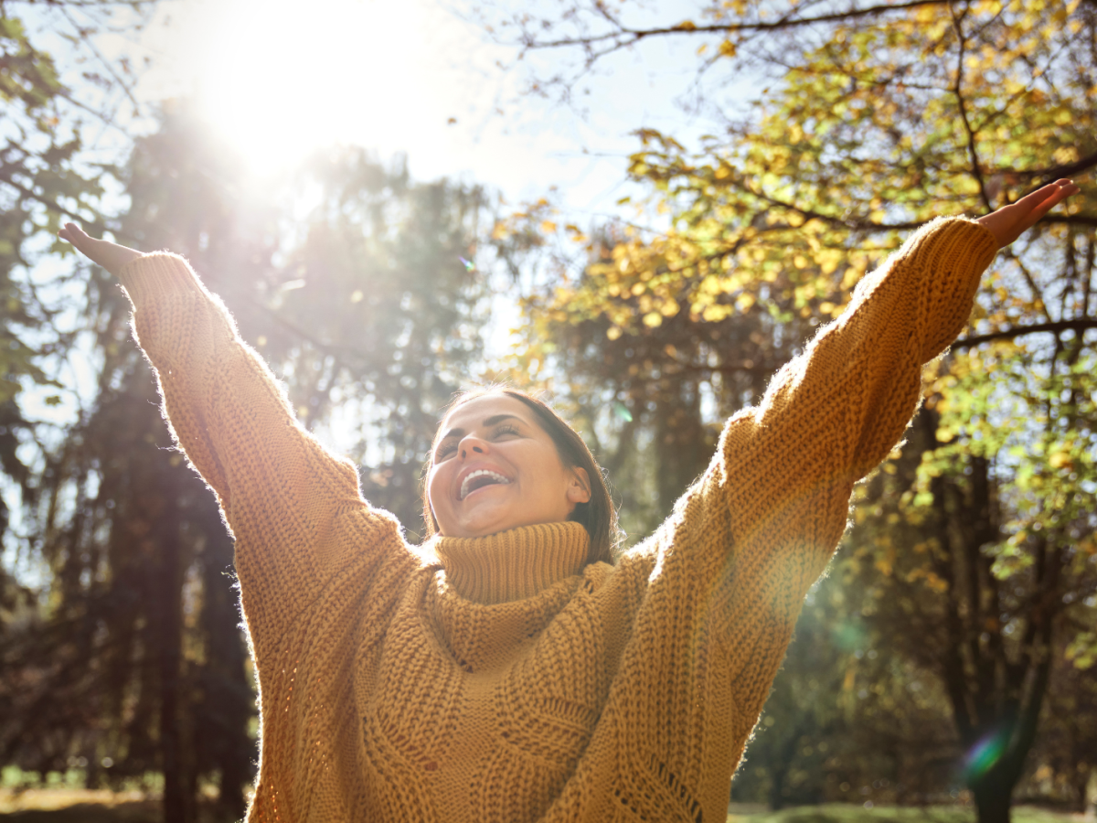 Frau im Wald, die gl&uuml;cklich ihre H&auml;nde in die Luft wirft und lacht.