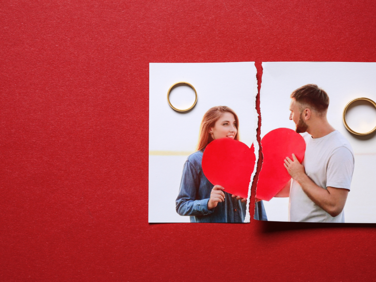 Zerrissenes Foto eines Paares mit rotem Herz auf rotem Untergrund, daneben zwei goldene Ringe als Symbol f&uuml;r Trennung.