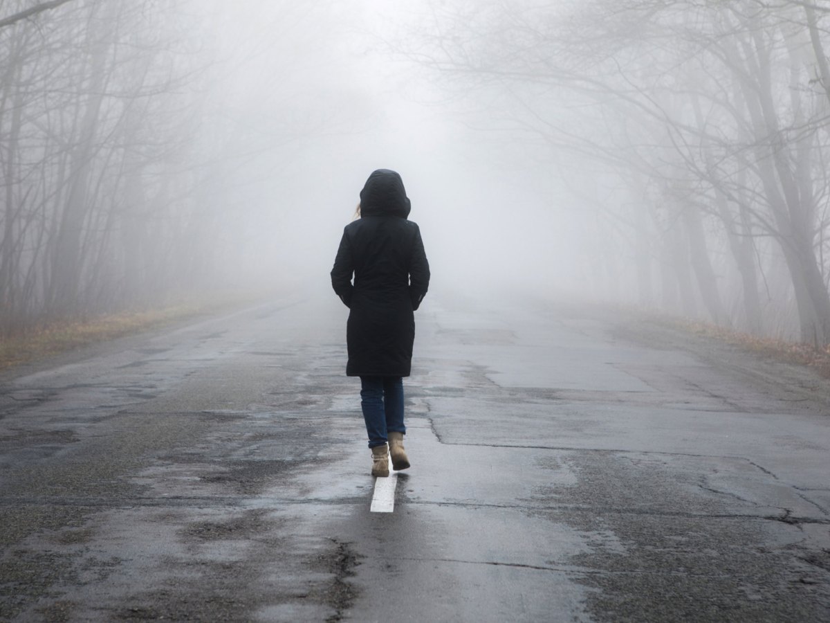 Frau mit Kapuze auf langer dunkler Stra&szlig;e