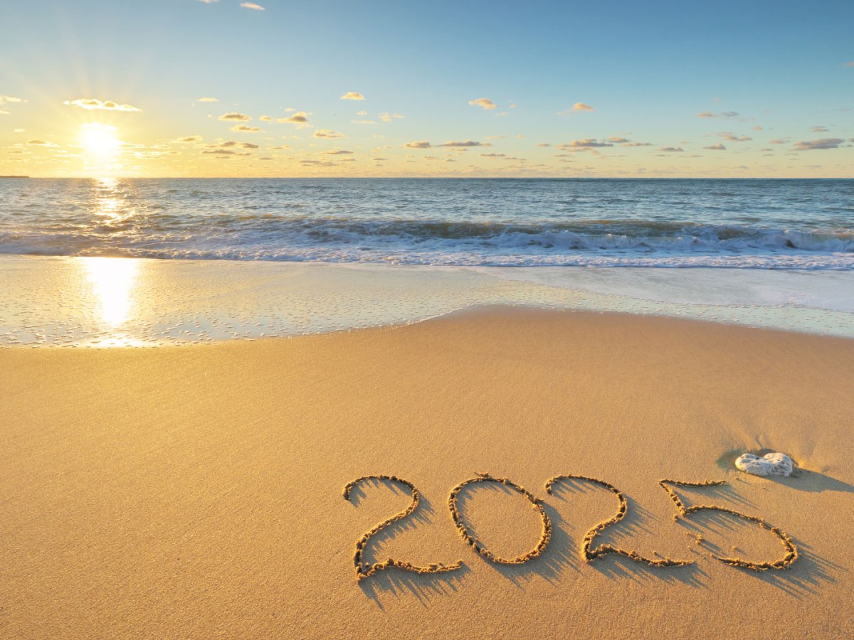 Sonnenuntergang an einem Strand, "2025" in den Sand gemalt.