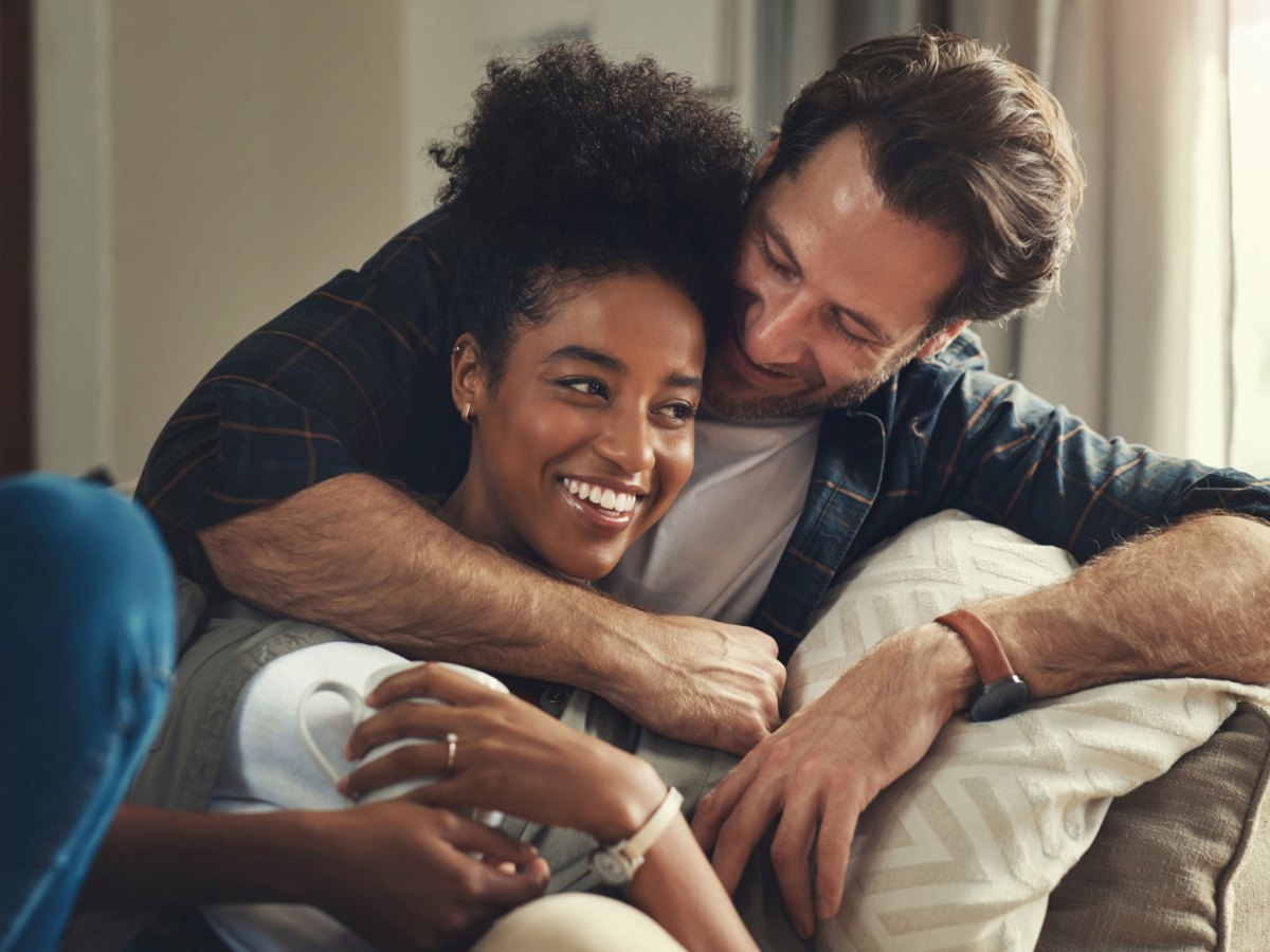 Frau und Mann zusammen auf dem Sofa, l&auml;cheln und umarmen sich
