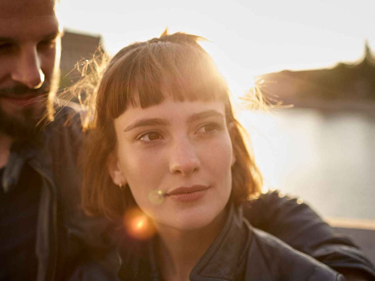 Junge Frau mit Bob guckt zur Seite, w&auml;hrend ihr Freund sie anguckt.