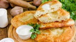 Mehrere Langosch, gestapelt auf Holzbrett, daneben ein Sch&uuml;sselchen mit Saurer Sahne.