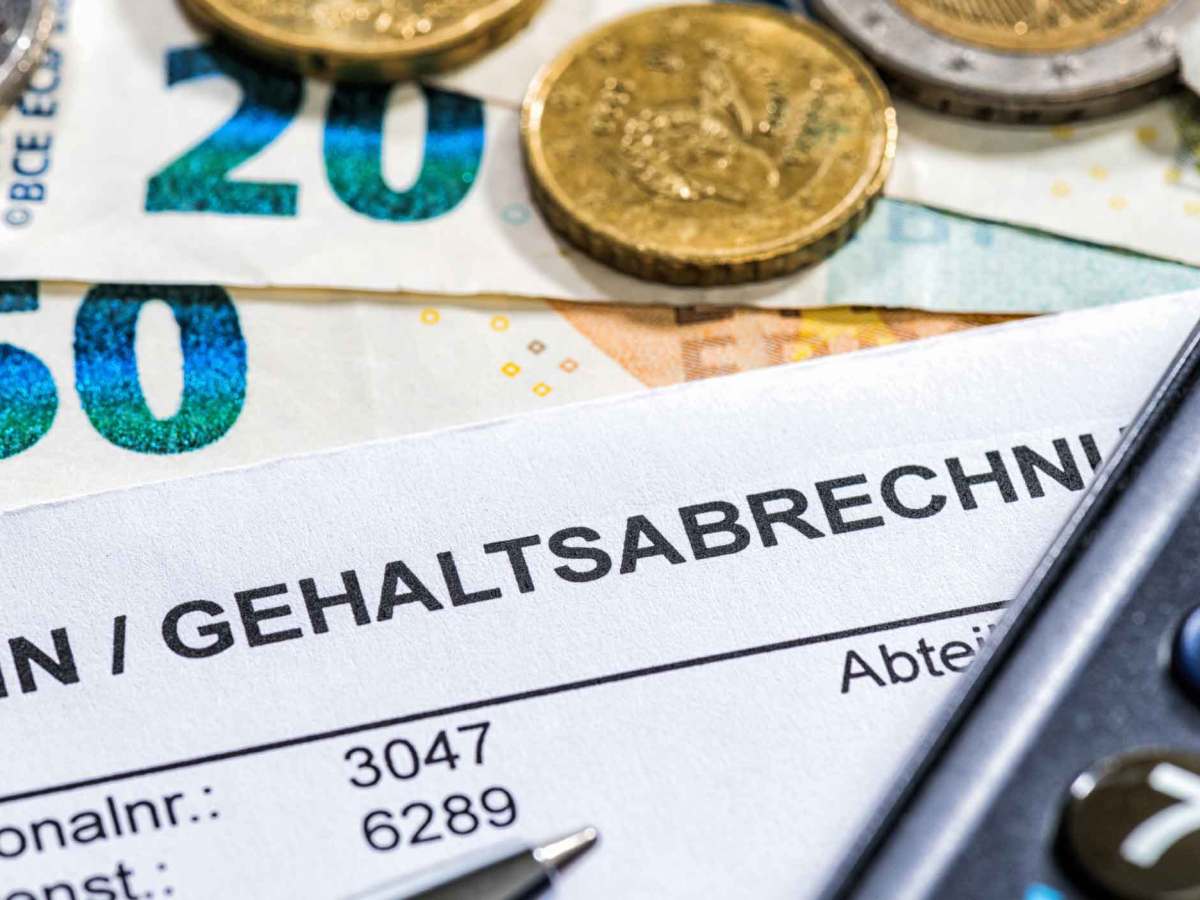Lohn-/Gehaltsabrechnung auf einem Tisch. Darauf liegen Geldscheine und M&uuml;nzen.