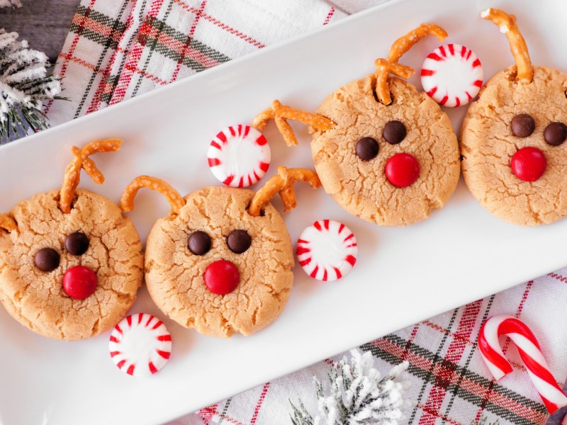 Kekse, mit Brezel als Geweih und roter Schokolinse als Nase auf einem weißen Teller.