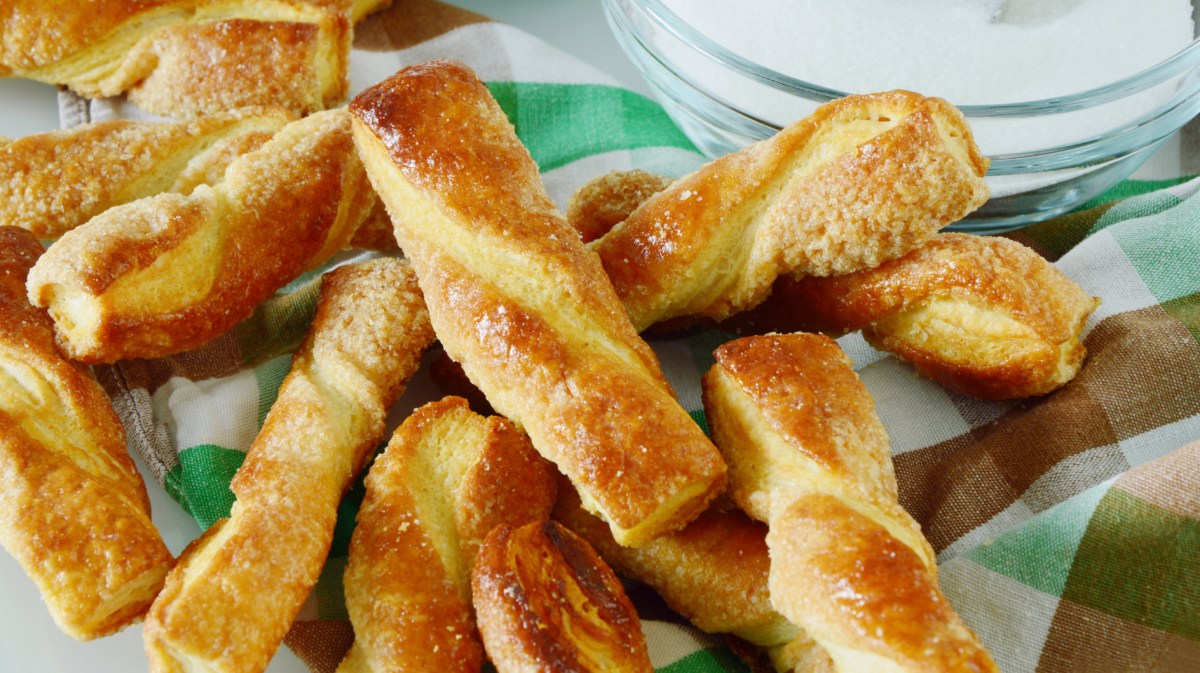 Blätterteigstangen mit Zucker auf einem hellen Küchentuch.