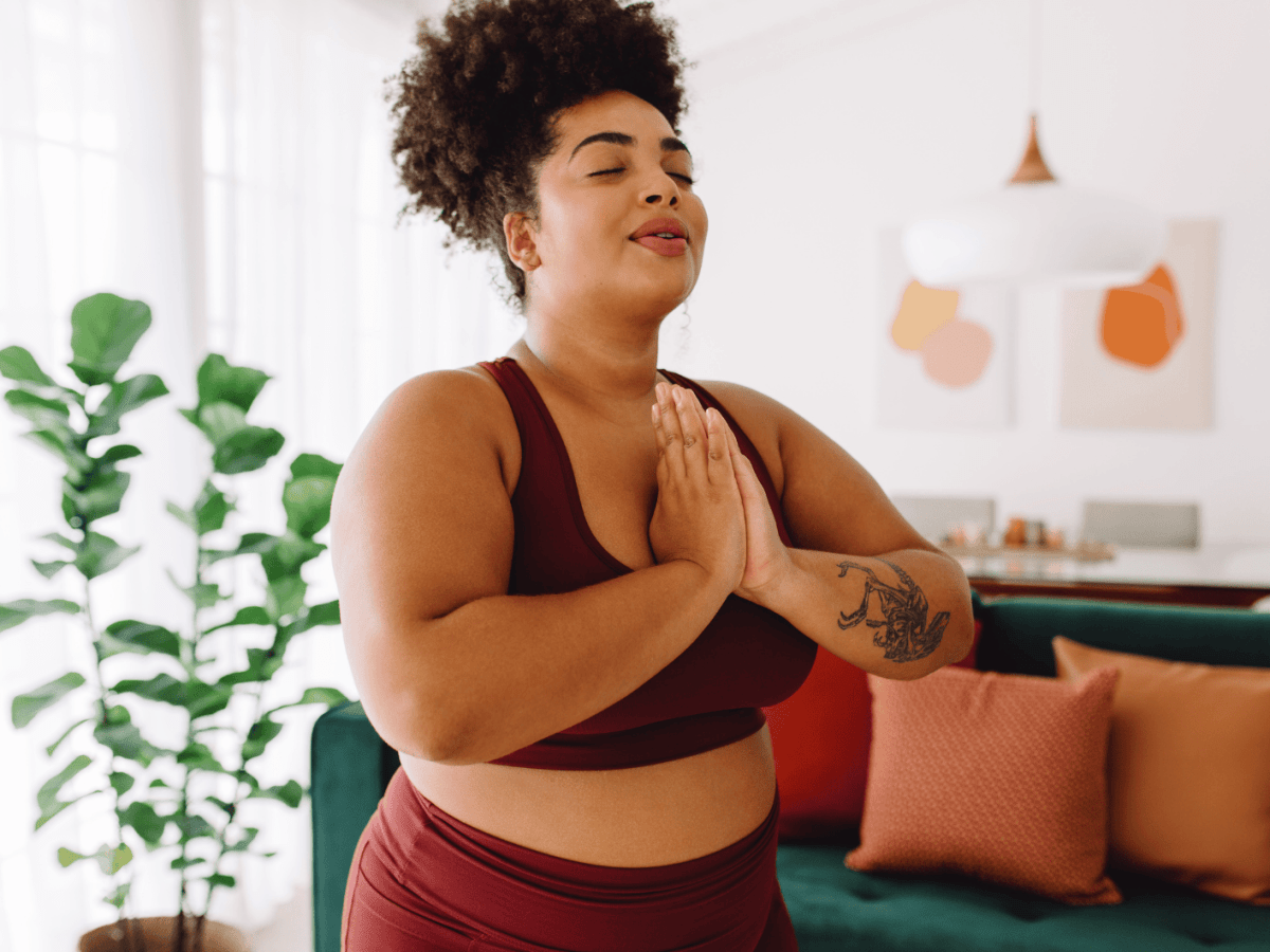 Frau vor Couch, die Yoga macht und die H&auml;nde vor der Brust zusammenlegt