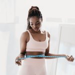 Unzufriedene junge Frau, die ihre Taille mit einem Maßband misst und sich über die Ergebnisse einer Schlankheitsdiät ärgert, weil sie nicht abnimmt