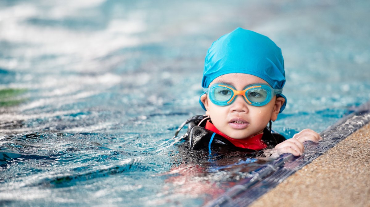 Kleines Mädchen mit Badekappe und Schwimmbrille im Schwimmbecken.