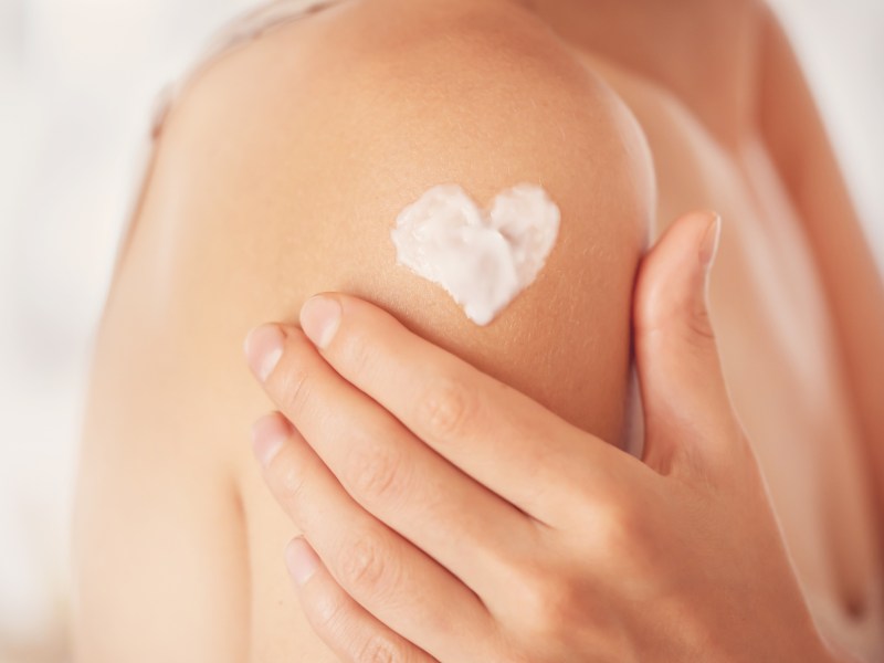 Frau cremgt sich die Schulter ein