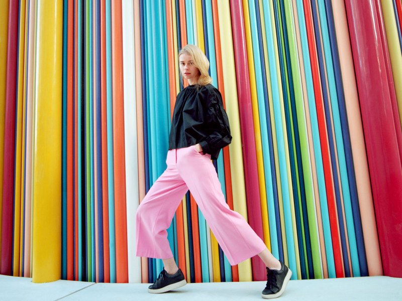 Frau läuft vor einer gestreiften, bunten Wand