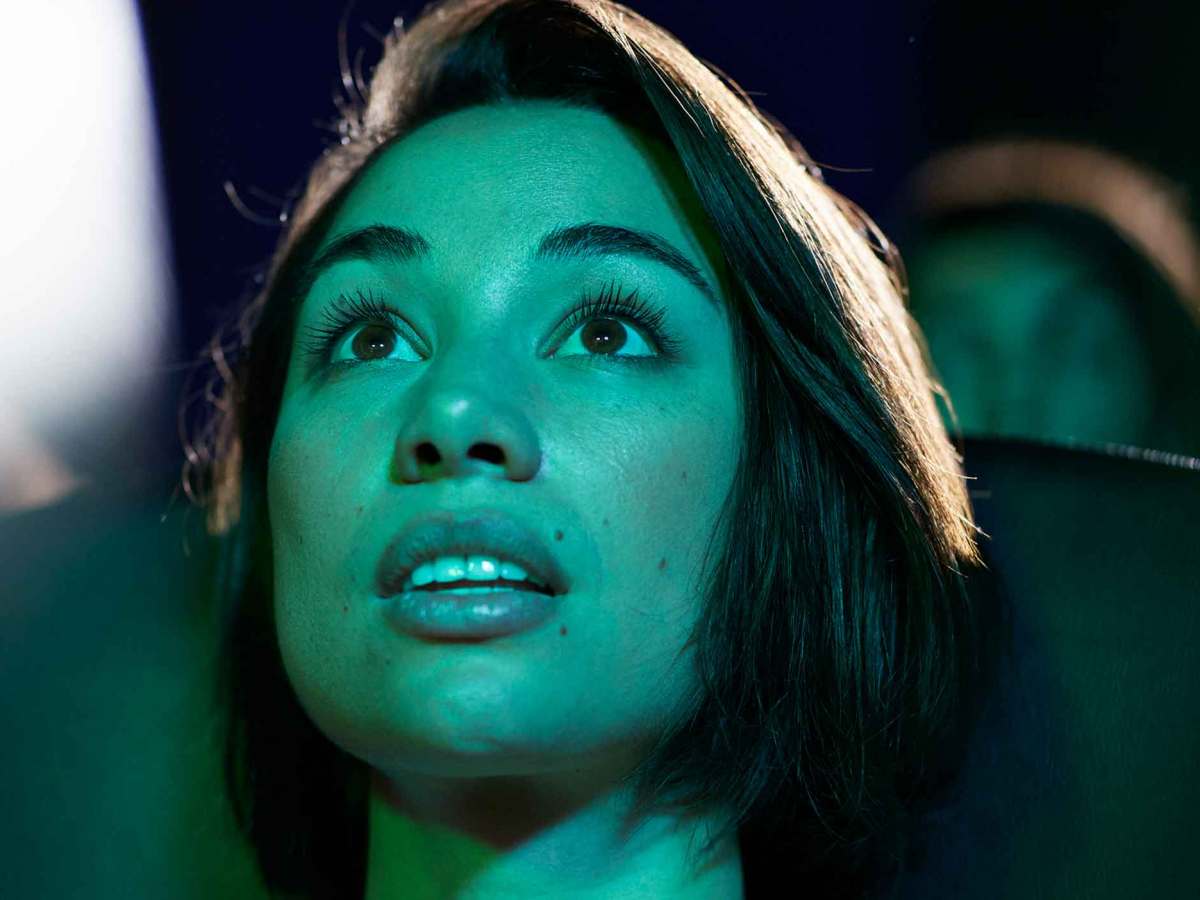 Junge Frau sitzt im Kino bei einem Horrorfilm und guckt erschrocken und gebannt.