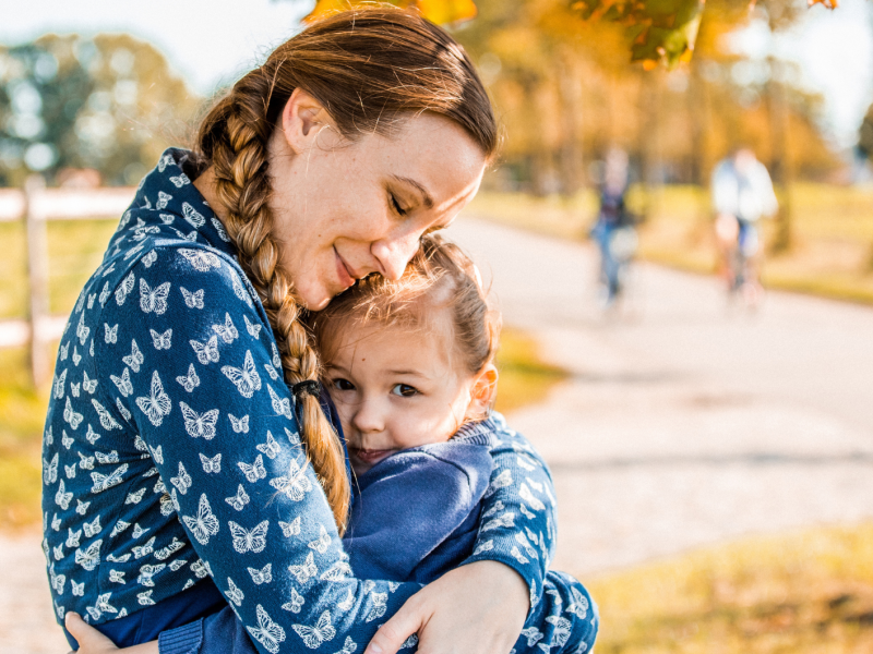 Mutter und Kind sitzen im Park auf einer Bank und umarmen sich