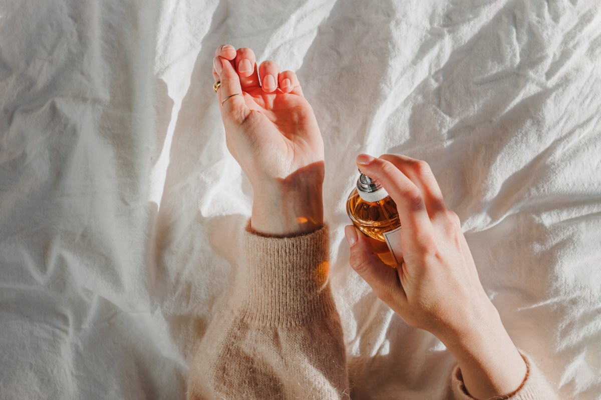 Frauenhände, die Parfum auf Handgelenk aufspürhen