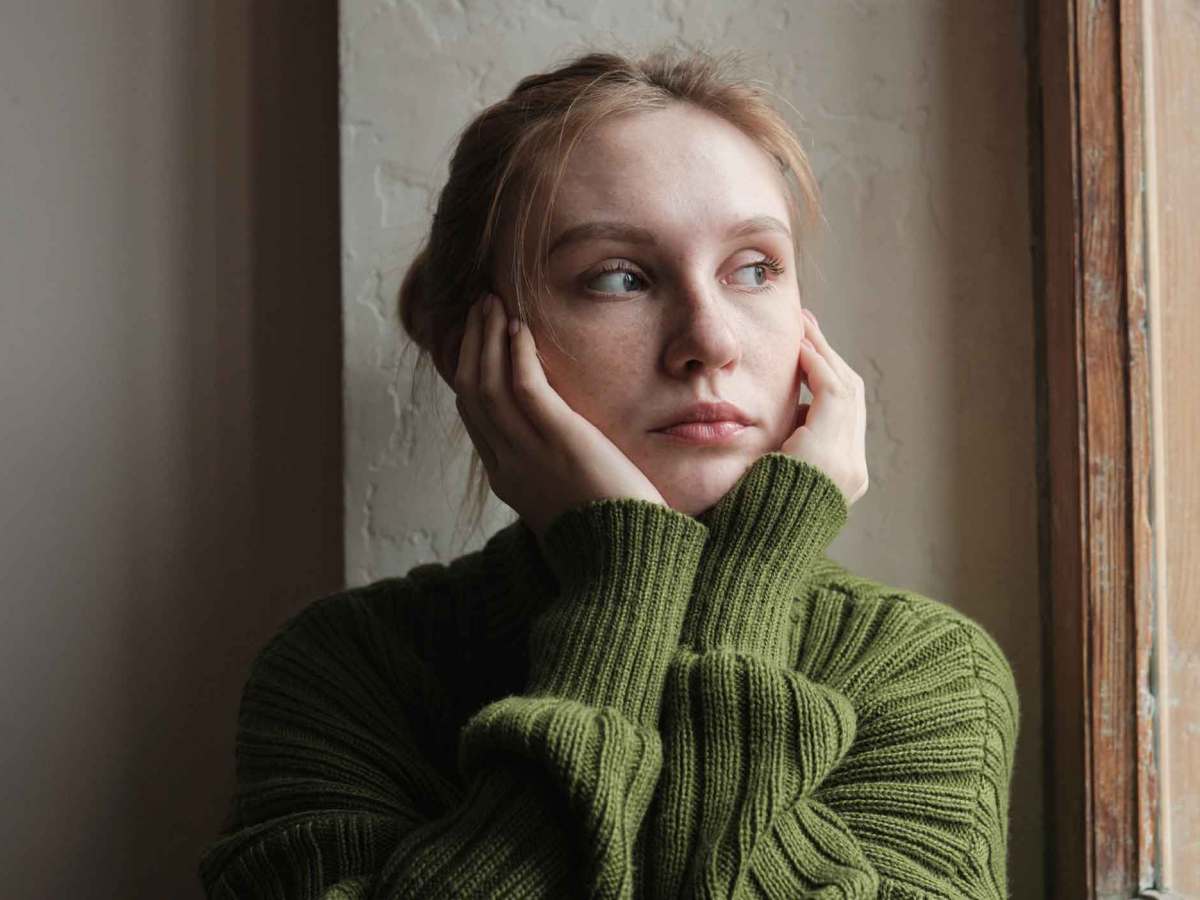 Junge Frau mit gr&uuml;nem Pullover guckt nachdenklich nach drau&szlig;en.
