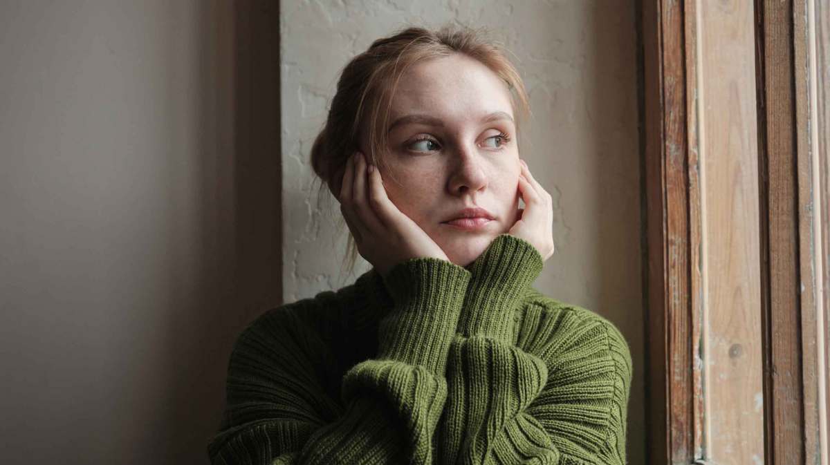 Junge Frau mit grünem Pullover guckt nachdenklich nach draußen.