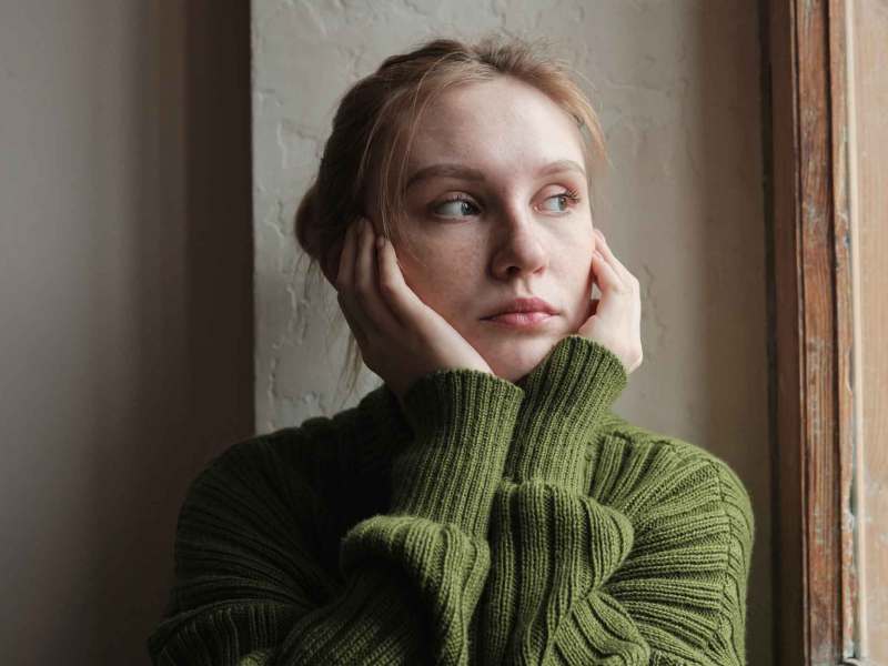 Junge Frau mit grünem Pullover guckt nachdenklich nach draußen.